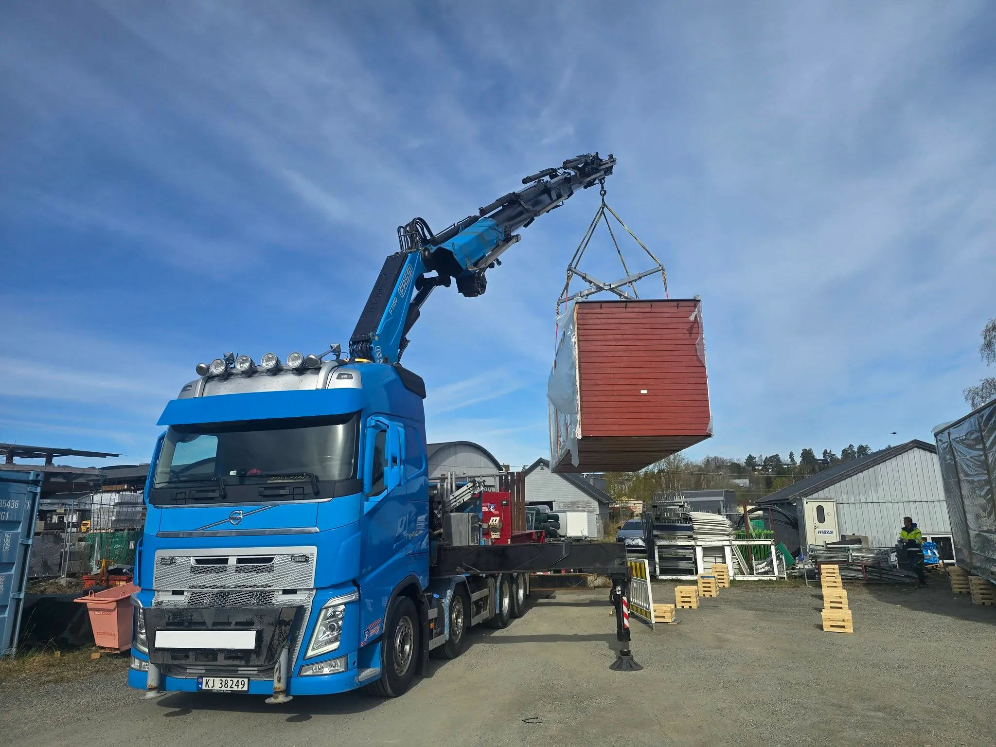 Blå Volvo kranbil fra Edwin Hoff AS løfter container med Fassi-kran